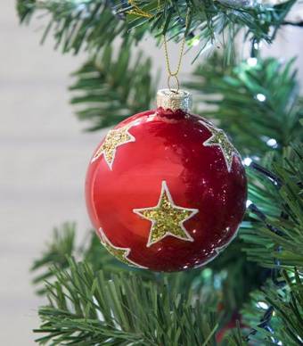 Bola vermelha com estrela dourada desenhada pendurada numa árvore de natal